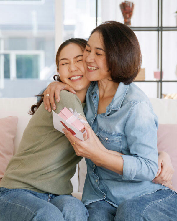 Mom and daughter sitting on a sofa. They're hugging as the mum is recieveing a Mother's Day gift.