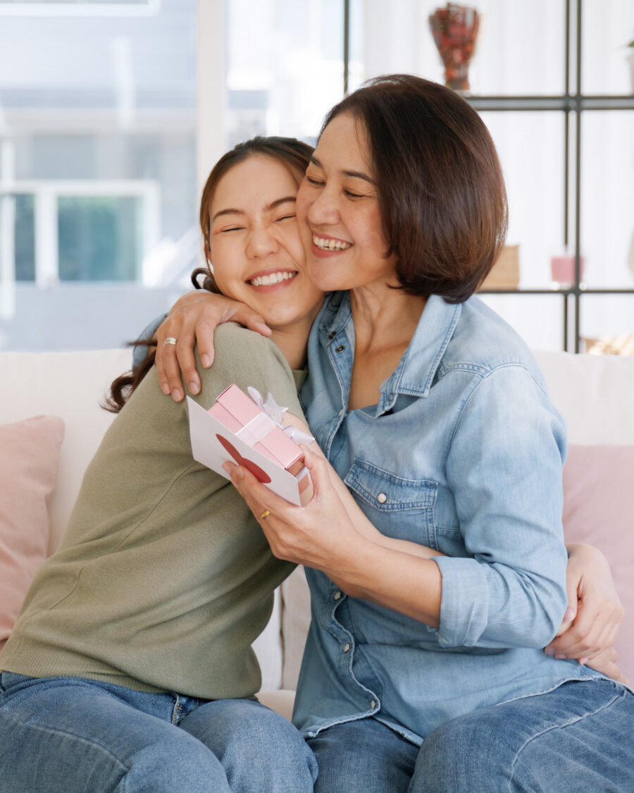 Mom and daughter sitting on a sofa. They're hugging as the mum is recieveing a Mother's Day gift.